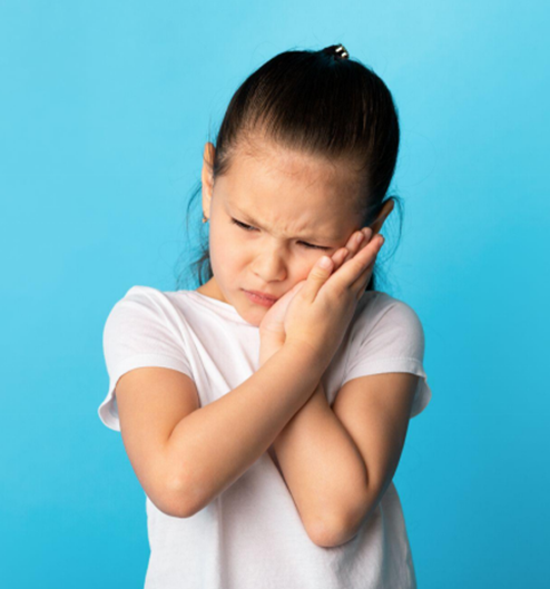 Young child in white shirt holding cheeks against blue background, appearing uncomfortable or in dental pain.