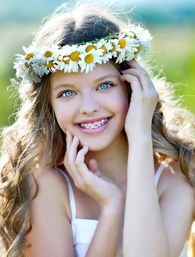 Young girl smiling wearing daisy flower crown outdoors in natural setting.