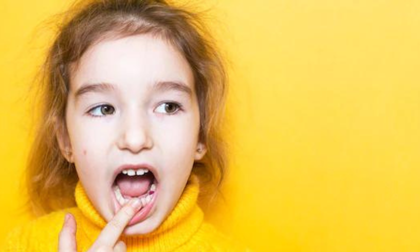 Young girl with finger in mouth against bright yellow background, playful dental expression.