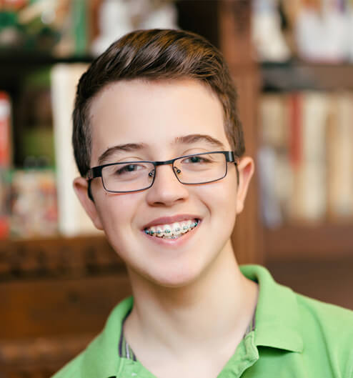 Young person wearing glasses and green shirt smiling in dental office library setting.