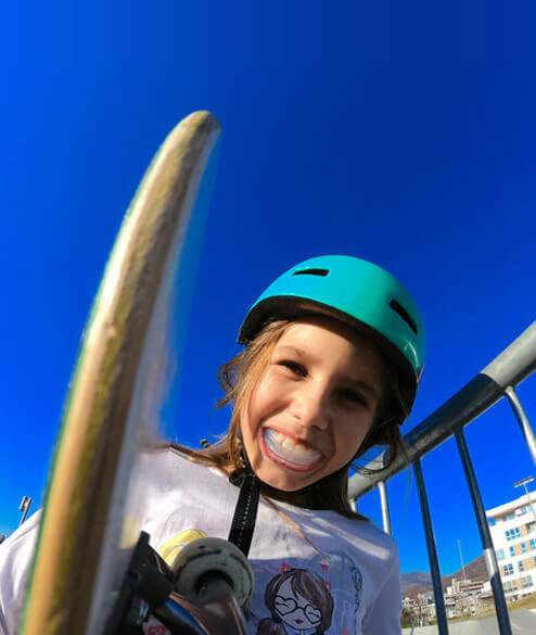 Child in green helmet and safety gear climbing playground equipment against blue sky.