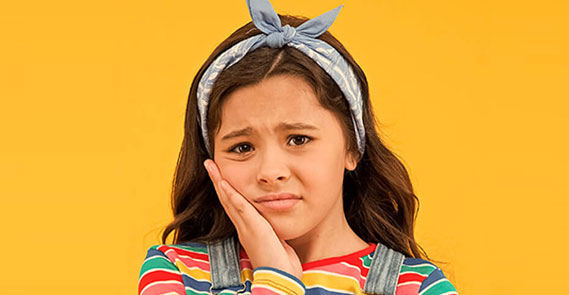 Young girl with headband smiling against yellow background for pediatric dental practice