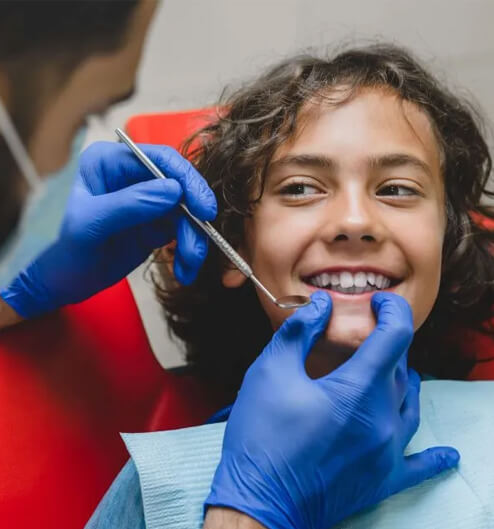 Young child smiling at dentist during dental examination wearing blue gloves in clinic.