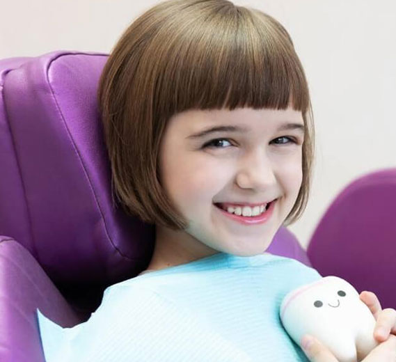 Young girl smiling in dental chair holding stuffed animal at orthodontic office.
