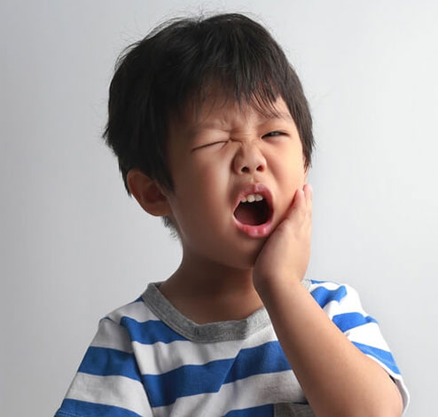 Young child in blue striped shirt holding cheek, appearing to have tooth pain or discomfort.