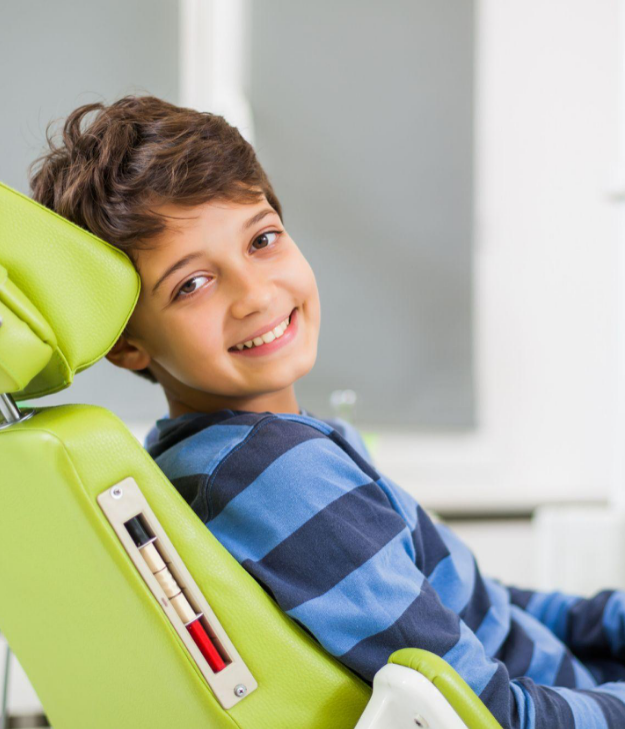 Young boy in blue checkered shirt smiling while sitting in dental chair at orthodontic office.
