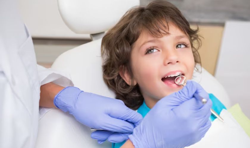 Young child at dental appointment wearing purple gloves, smiling in dentist's chair during checkup.